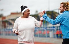 Male personal trainer high fiving woman on outdoor track